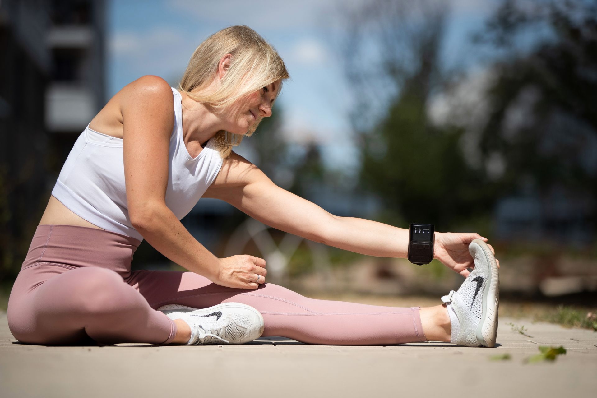 A woman sitting on the floor in sportswear and stretching while wearing an EndoLight® band on her arm