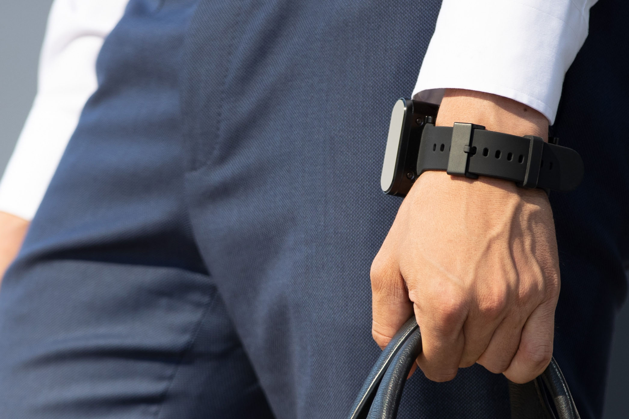A person wearing a white shirt and blue trousers is holding a black bag. He is wearing a black EndoLight® strap on his wrist.